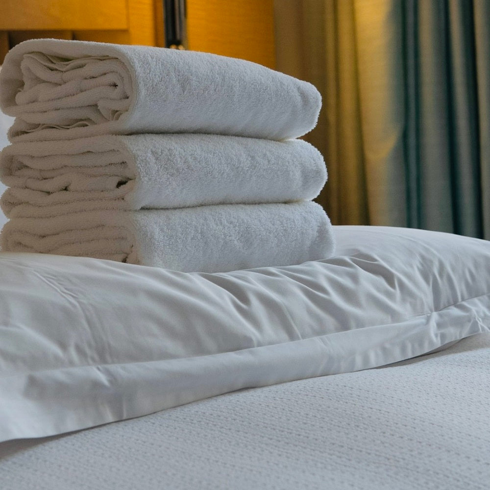 Stack of white towels on a bed with curtains in the background