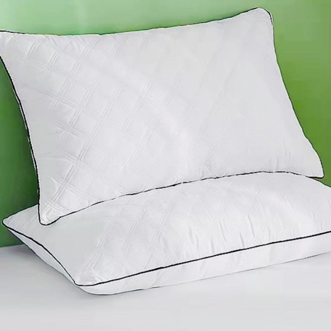 Two white pillows with black piping on a bed against a green wall.